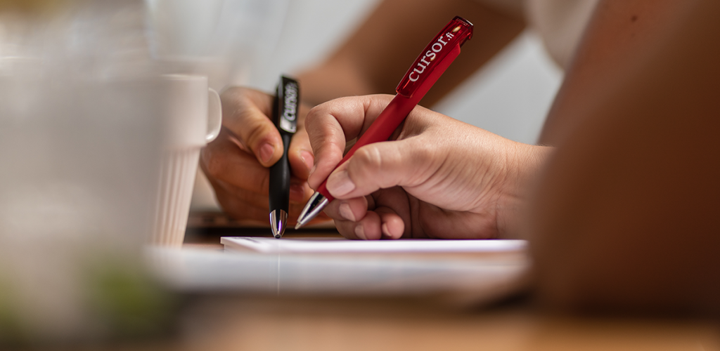 Kaksi kättä kynät kädessä kirjoittamassa valkoiselle paperille.