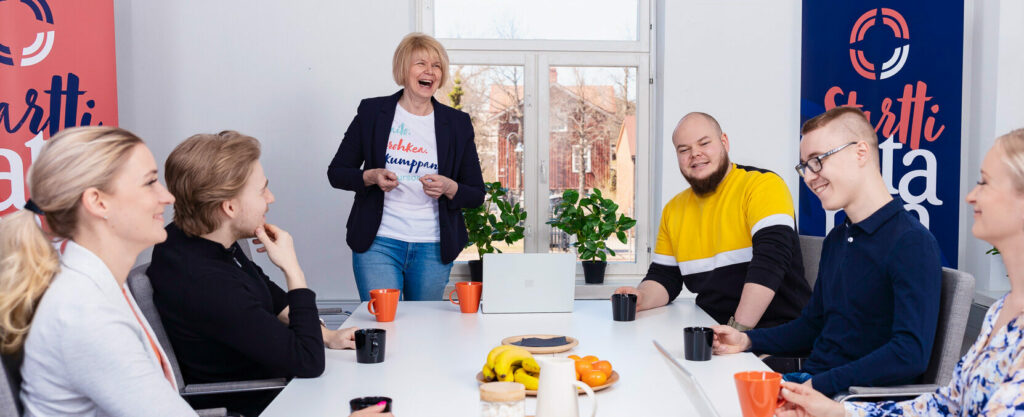 Ihmisiä valkoisen kokouspöydän ääressä nauramassa.