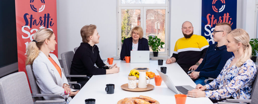 Ihmisiä kokouspöydän ääressä keskustelemassa.